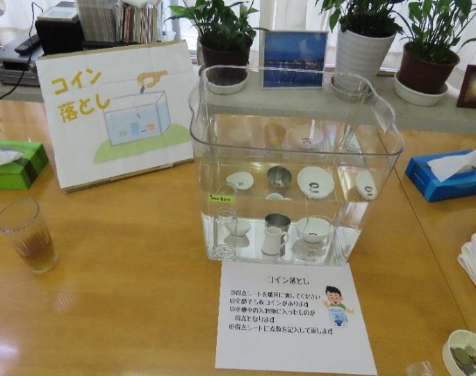 夏祭りのコイン落としゲームです。水を張った水槽の底に4つの小さなコップが置かれており、コップを目がけてコインを落とすゲームです。